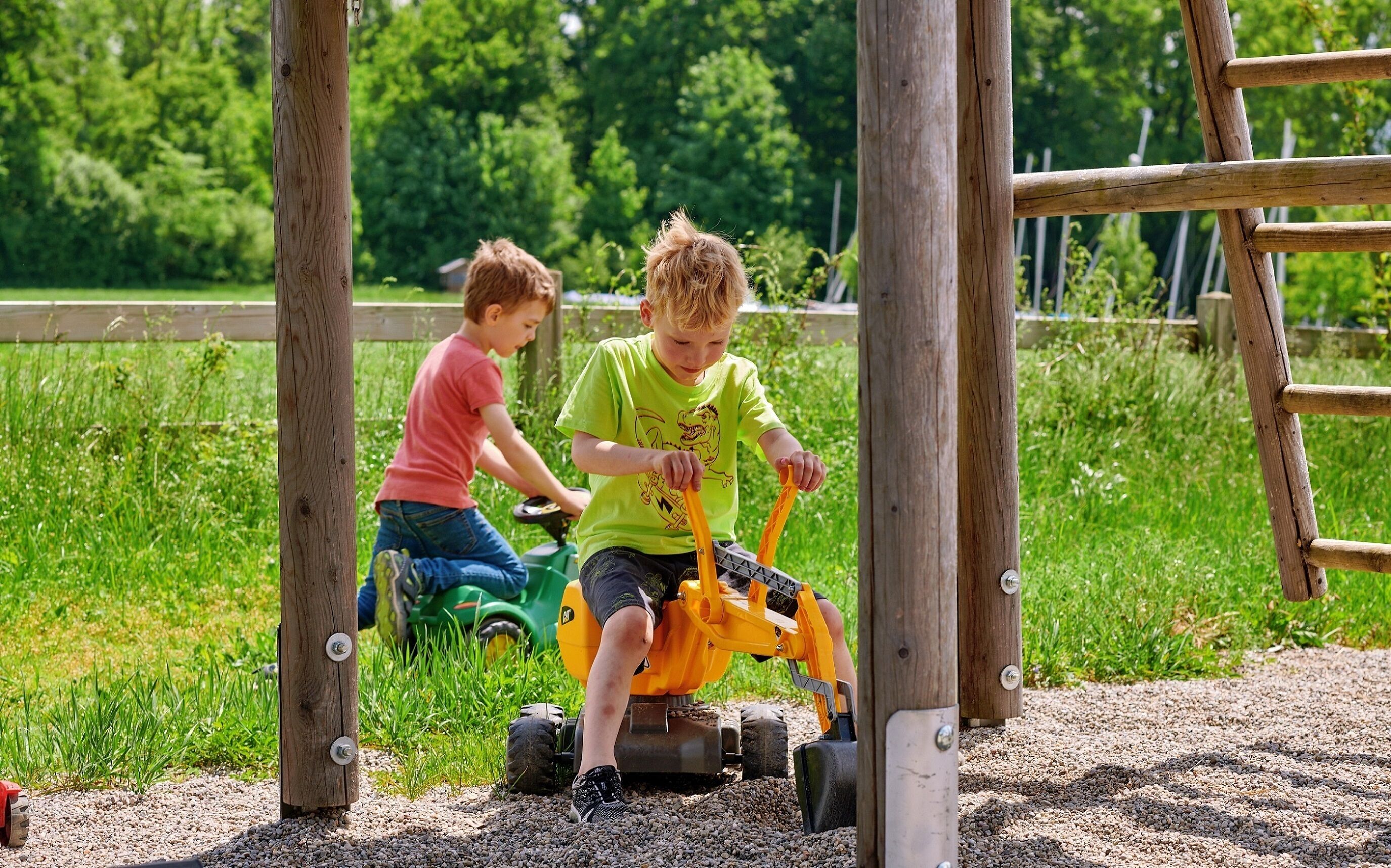 Dos niños jugando con un tractor de juguete en un camino de grava.