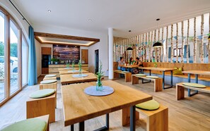 Un restaurant moderne avec des tables et des bancs en bois, de grandes fenêtres et une vue sur l’extérieur.