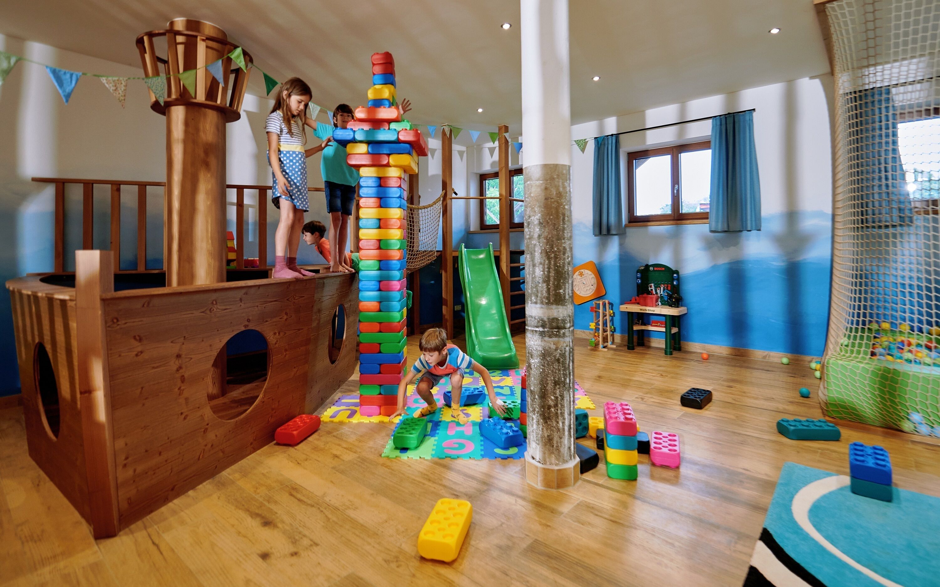 A play area with a wooden ship play structure, a slide, and various play mats and toys.