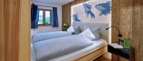 Un dormitorio moderno con cabecera de madera, dos camas con sábanas blancas, una mesita de noche con lámpara y un mural de peces en la pared.