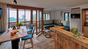 Ein moderner, offener Wohn- und Essbereich mit Holzboden, einem mit Gläsern und Teekanne gedeckten Esstisch, einer Couch mit Kissen sowie einer Küchenzeile mit Mikrowelle und Kaffeemaschine.