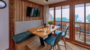 Ein Holztisch mit einer Bank, ein an der Wand befestigtes Fernsehgerät und ein Blick ins Freie durch große Fenster.