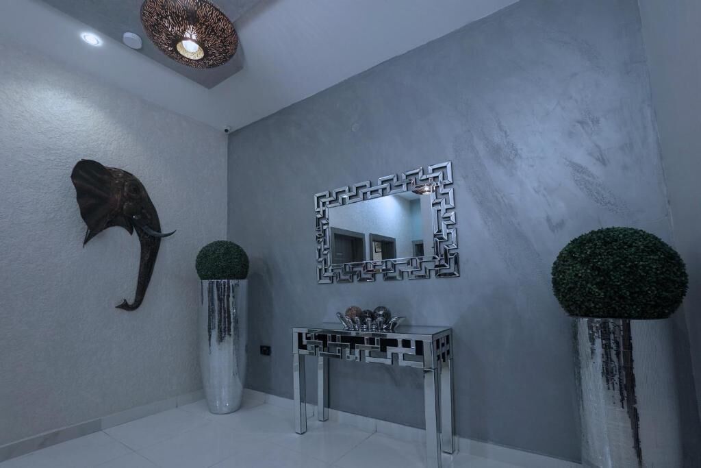 A modern bathroom with a grey wall, a decorative mirror, a sink, and two potted plants.