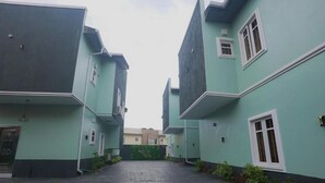 A courtyard with buildings having a uniform exterior design, featuring a central pathway and small plants along the edges. - 3H Villas Hotel & Luxury Apartment (Lekki)