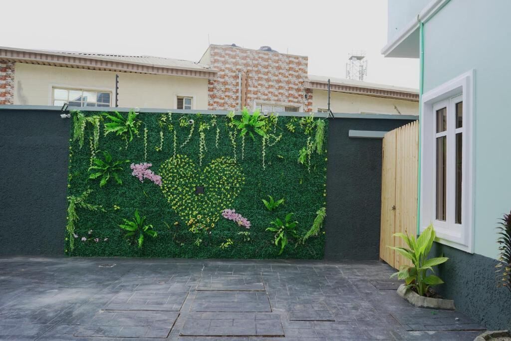 A courtyard with a green wall covered in plants and flowers, a paved floor, and a wooden fence.