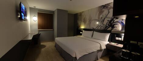 A modern hotel room with a large bed, a TV mounted on the wall, a window with a view, and a wall-mounted light fixture.