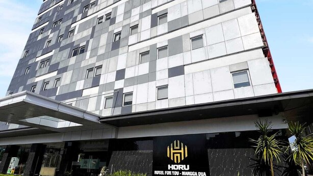 Een modern hotelgebouw met een opvallend logo en naam op de gevel.