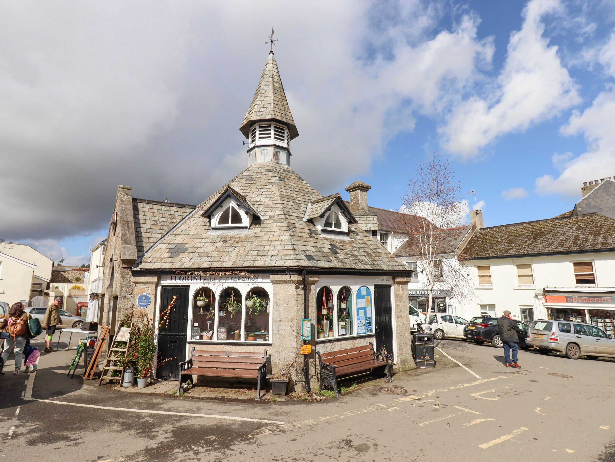 Un petit bâtiment en pierre, doté d’un toit en forme de flèche et d’un clocher, entouré de voitures garées et de piétons.