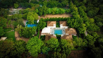 Vista aérea de una propiedad con piscina, varias edificaciones y follaje circundante.