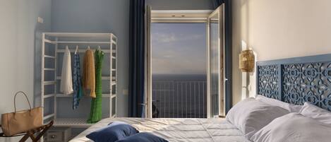 A bedroom with a bed, a wardrobe, a suitcase, and a view of the sea.