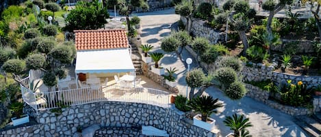 Zona de piscina con sillas de descanso, pared de piedra y vistas a una casa con tejado rojo y balcón.