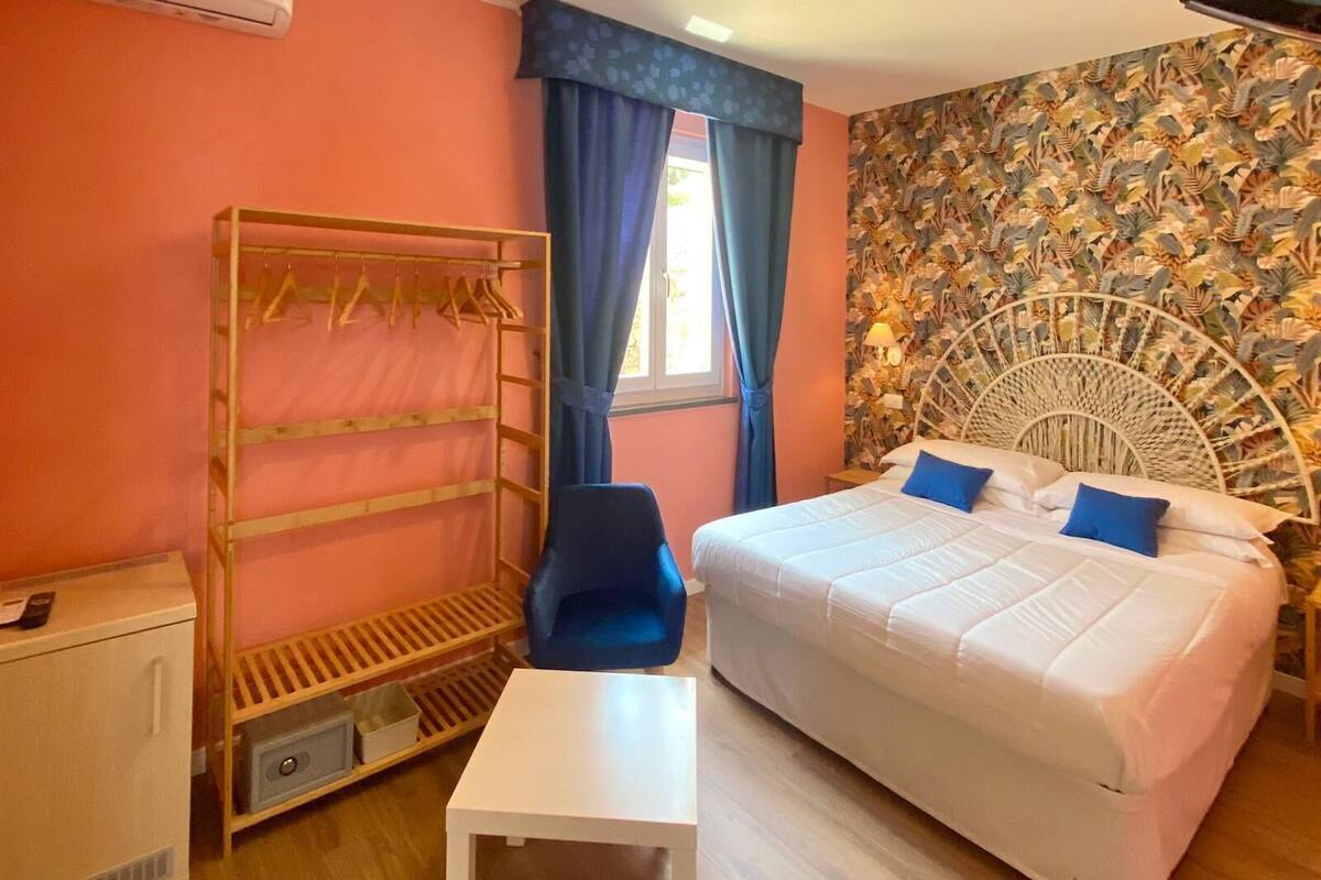Ein Schlafzimmer mit Bett, Stuhl, kleinem Tisch, Kleiderschrank und einem Fenster mit Vorhängen.