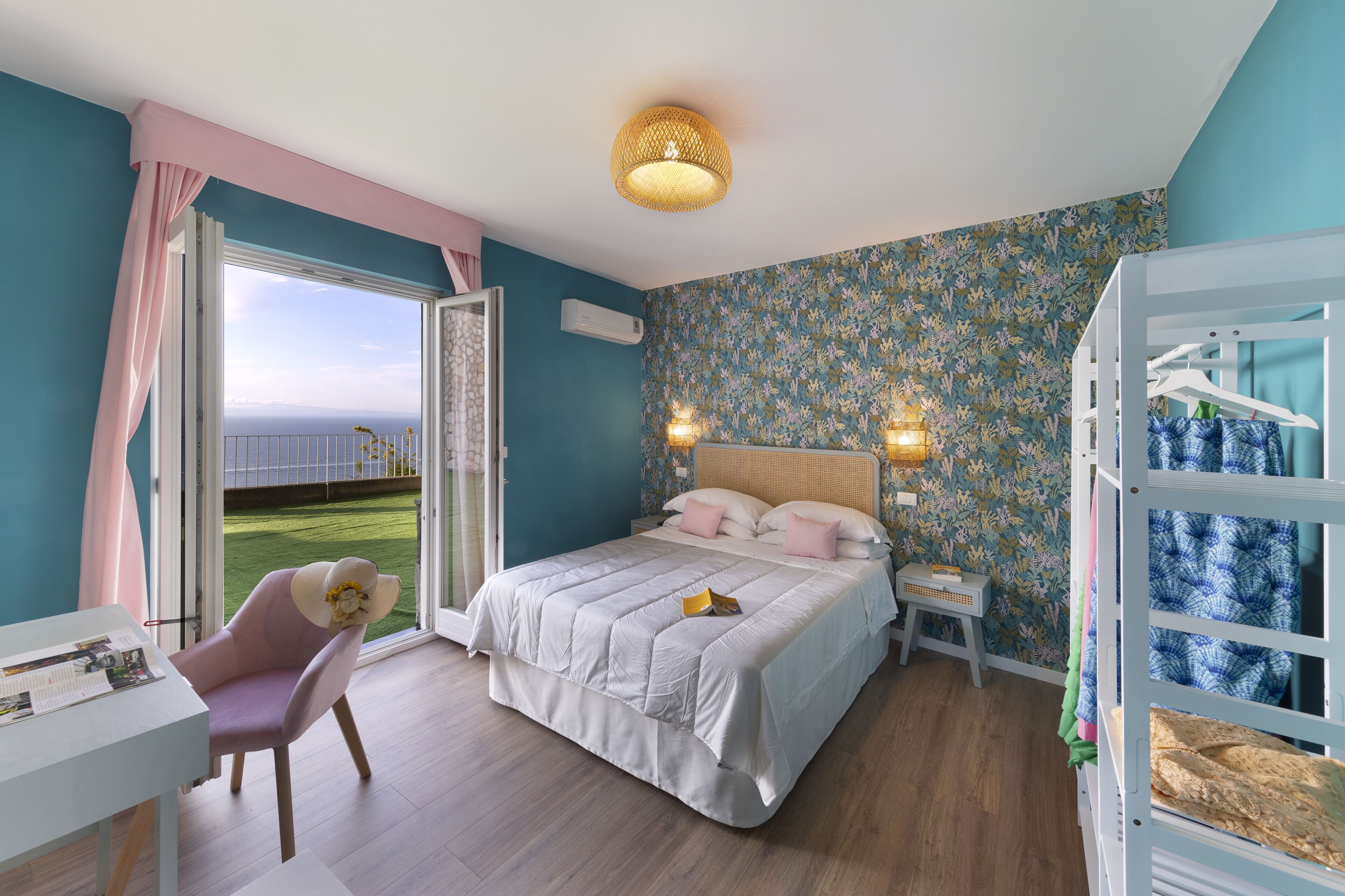 Un dormitorio con una cama grande, un escritorio y una silla. Se ve un paisaje verde a través de la ventana.
