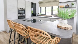 Et moderne køkken med en central ø, barstole, indbyggede ovne og et stort vindue med udsigt.