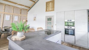 Et moderne køkken med en stor ø, rustfrit stål hvidevarer og et spiseområde med fletstole og en potteplante.
