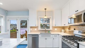 A modern kitchen with white cabinets, a stainless steel stove, and a microwave. - Skyline Blue House in Greenwood (Seattle)