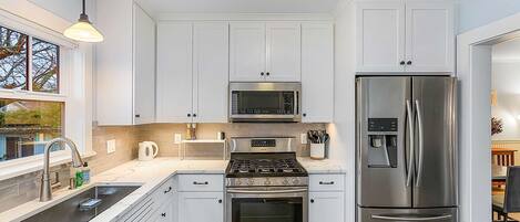 Eine moderne Küche mit weißen Schränken, Edelstahlgeräten, einer integrierten Mikrowelle, einem Backofen und einem Kühlschrank.