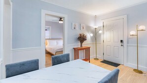 A hotel room with a bed, a dining table with chairs, a vase with flowers, a floor lamp, and a door. - Skyline Blue House in Greenwood (Seattle)