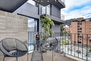 A balcony with two black wire chairs and a glass table, overlooking a street with buildings and a mountain in the background. - w* | Charming Loft with terrace in El Nogal (Bogotá)