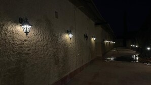 A nighttime corridor with textured walls and evenly spaced wall-mounted lights. - Mangalam Inn By AAA Grand (Shahpur)