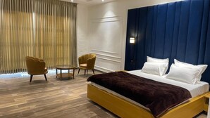 A modern hotel room with a large bed, two armchairs, a small round table, and a large window with curtains. - Mangalam Inn By AAA Grand (Shahpur)