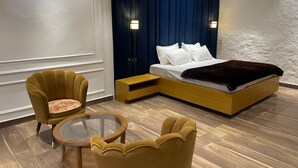 A modern hotel room with a large bed, a small side table, two armchairs, and a glass coffee table. - Mangalam Inn By AAA Grand (Shahpur)