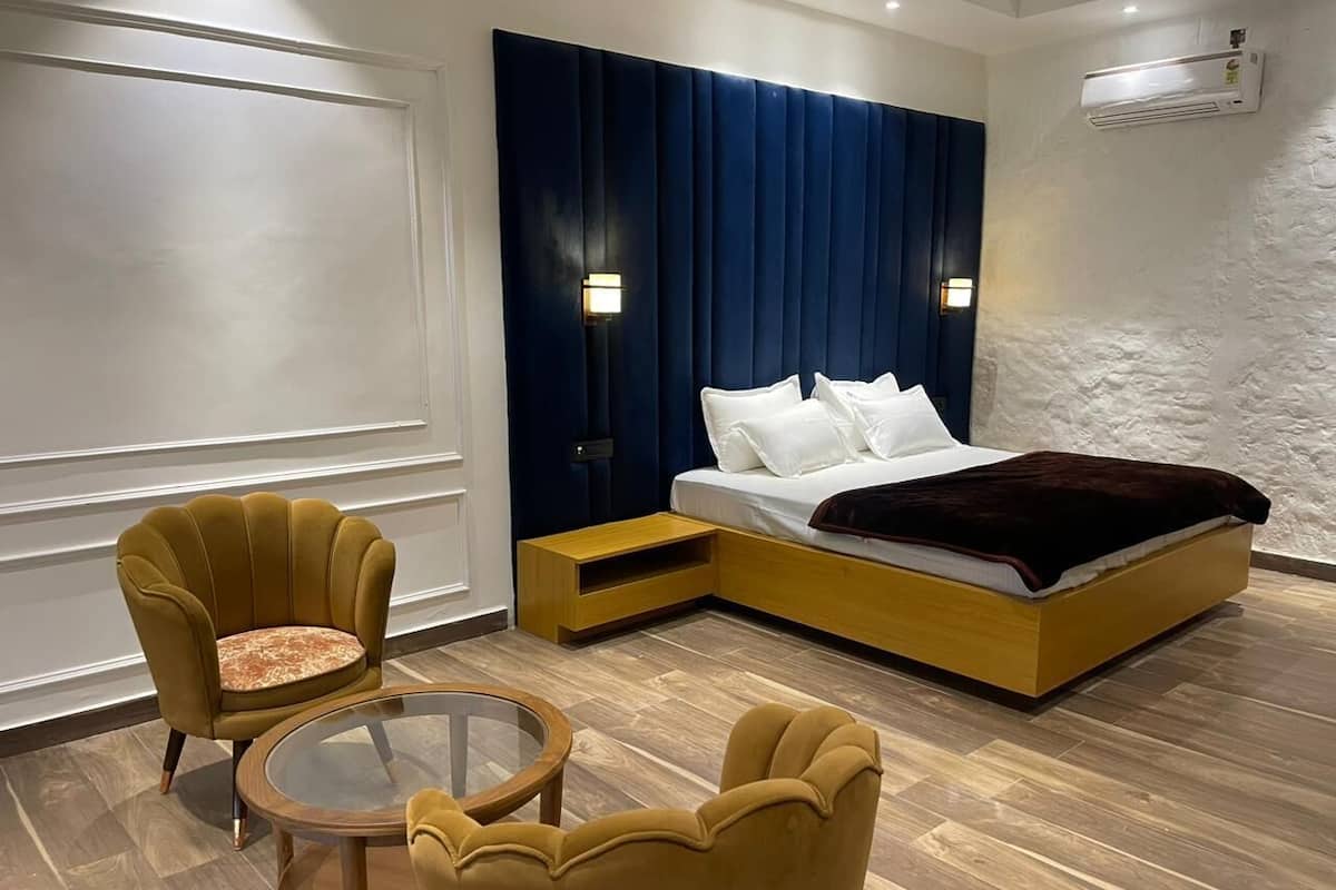 A modern hotel room with a large bed, a small side table, two armchairs, and a glass coffee table.