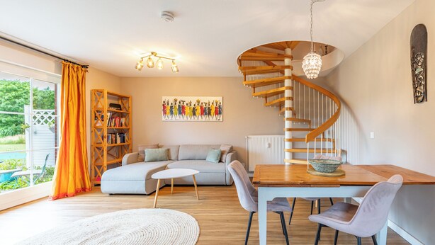 Ein modernes Interieur mit Wendeltreppe, Essbereich und Wohnbereich inklusive Sofa und Bücherregal.