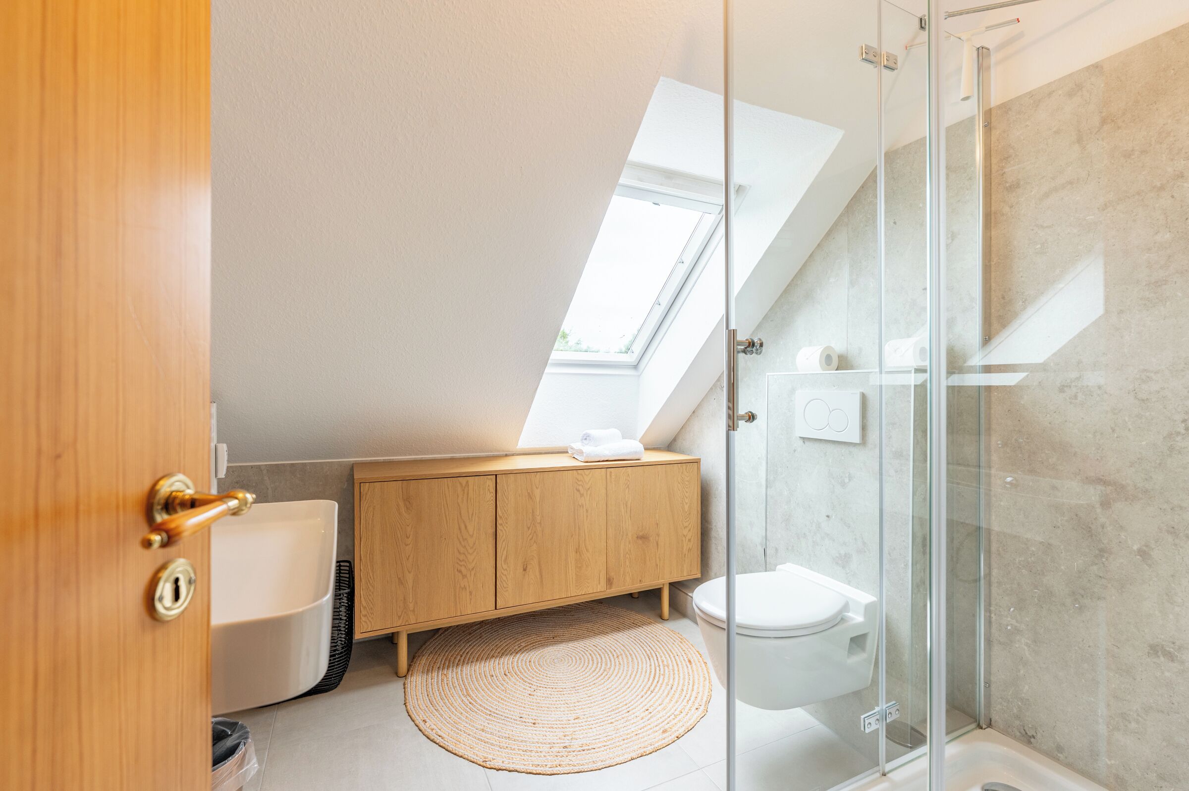 Ein modernes Badezimmer mit Oberlicht, einem Holzbadezimmer-Möbel, einer Toilette und einer Duschkabine aus Glas.
