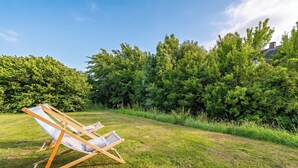 Eine grüne Wiese mit einem Holzstuhl und einem Haus im Hintergrund.