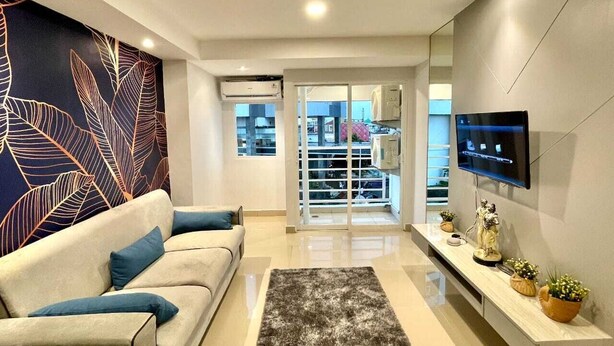 A modern living room with a sofa, a flat-screen TV, decorative items, and a large window. -  Alhesa Apartment Mansyur Residence (Medan)