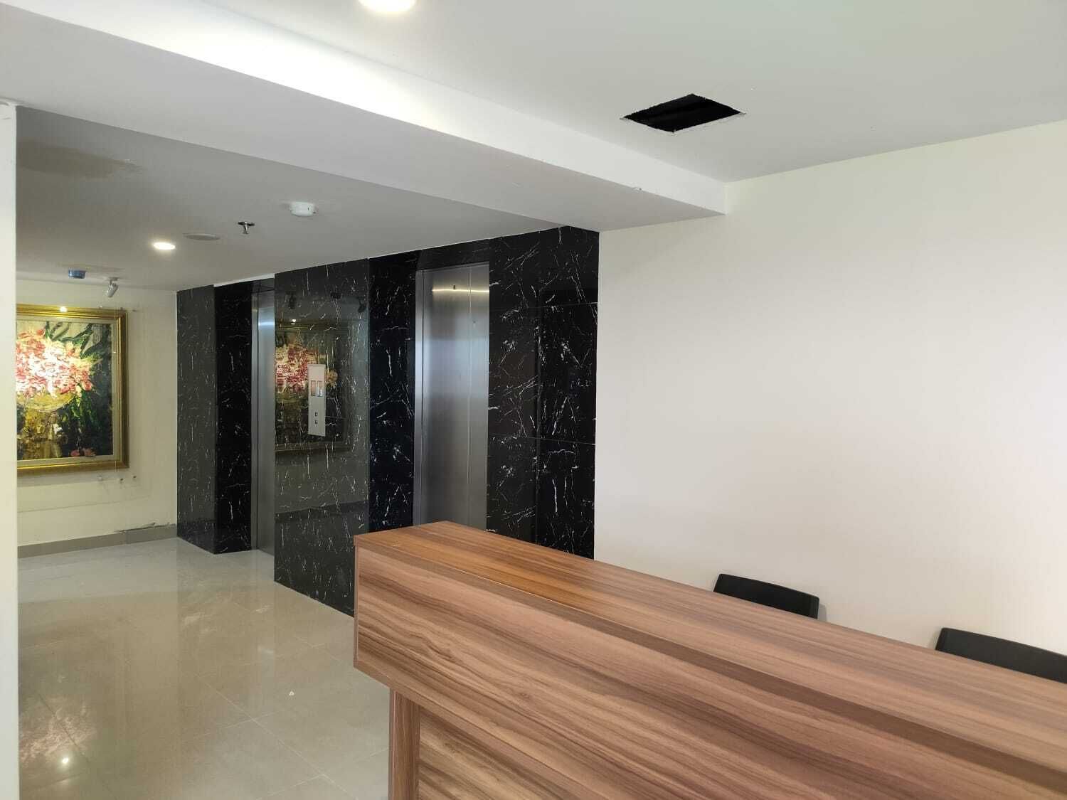 A modern reception area with a wooden reception desk, black marble walls, and a glass elevator.