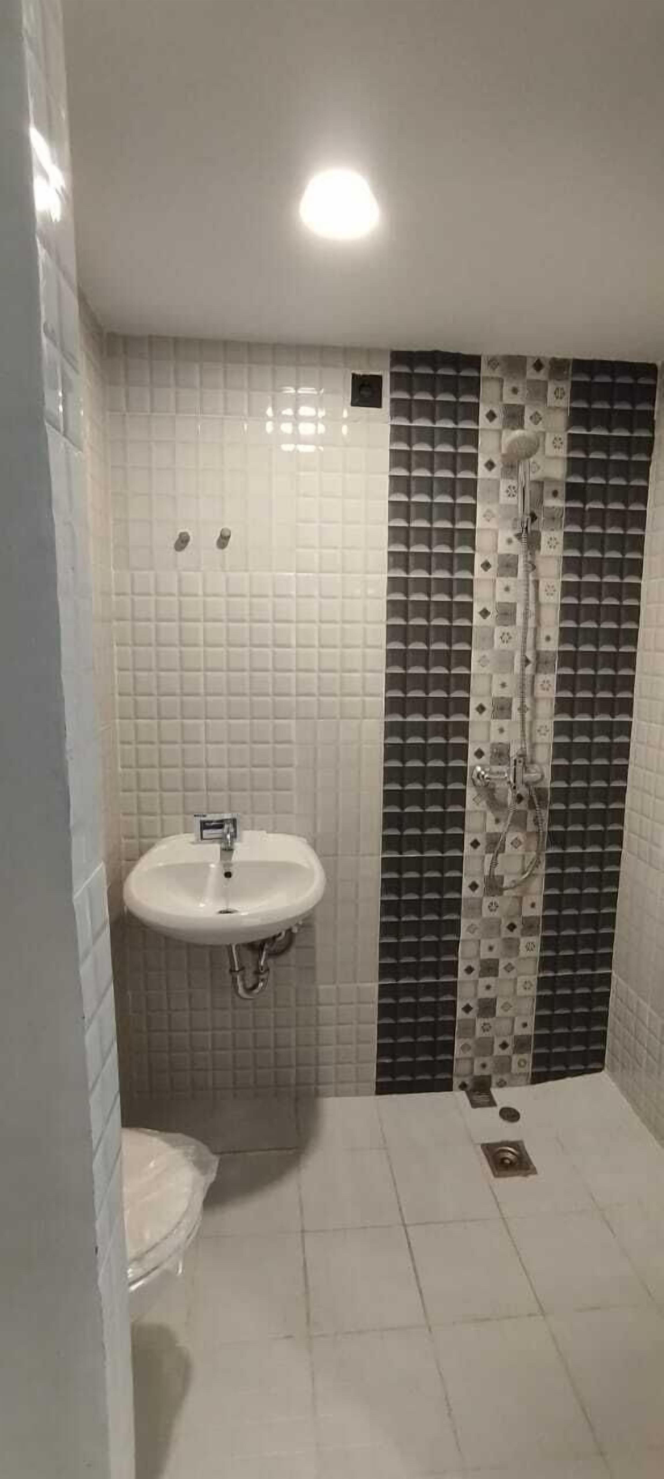 Un baño con lavamanos blanco, ducha y paredes de azulejos.