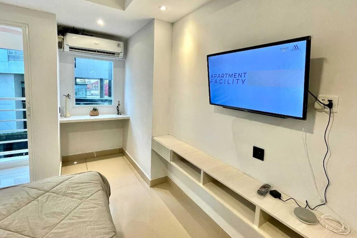 Un apartamento moderno con una televisión de pantalla plana montada en la pared, un banco empotrado y un ventanal con vistas a la calle.