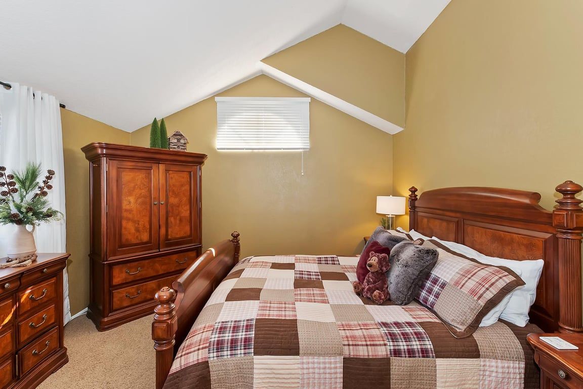 Une chambre à coucher avec un lit en bois, une table de chevet, une commode et une fenêtre avec des stores.