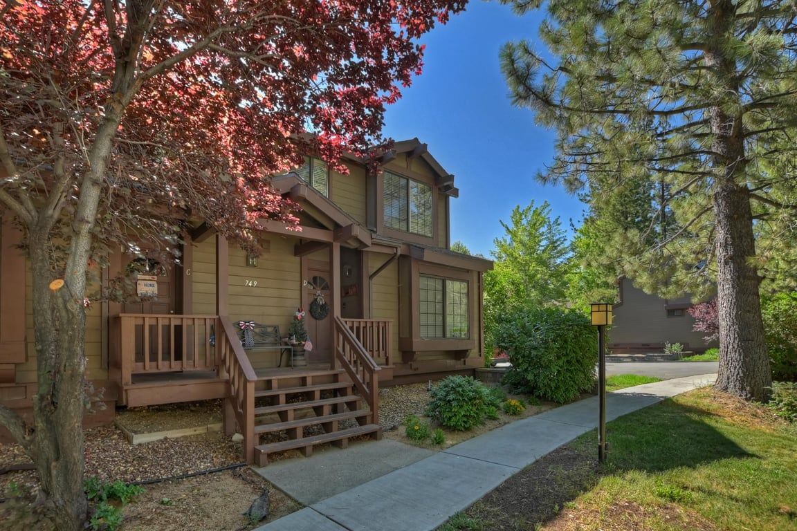 A two-story house with a front porch, a mailbox, and a street sign.