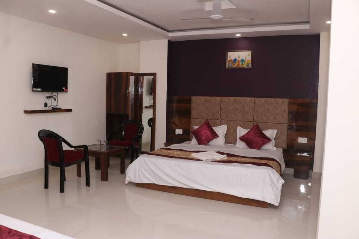 A hotel room with a large bed, a TV mounted on the wall, a desk with a chair, and a mirror.