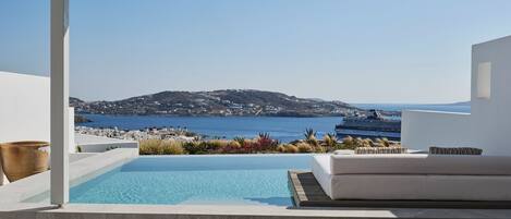 A modern outdoor seating area with a pool, overlooking a coastal landscape with a cruise ship in the distance.