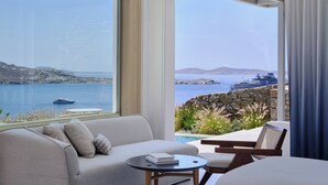 Une chambre moderne avec une grande fenêtre donnant sur une étendue d’eau et un yacht. On y trouve un canapé, une petite table ronde et une chaise.