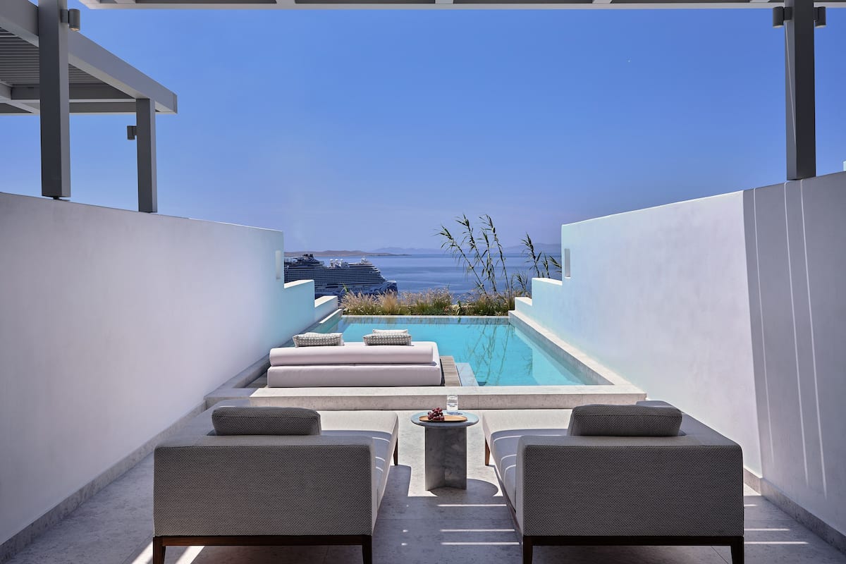 Un espace piscine aménagé sur le toit, avec deux chaises longues et une petite table, d’où l’on peut admirer un plan d’eau et un navire de croisière.