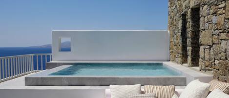 A modern outdoor pool area with a view of the sea, a stone wall, and a white infinity pool.