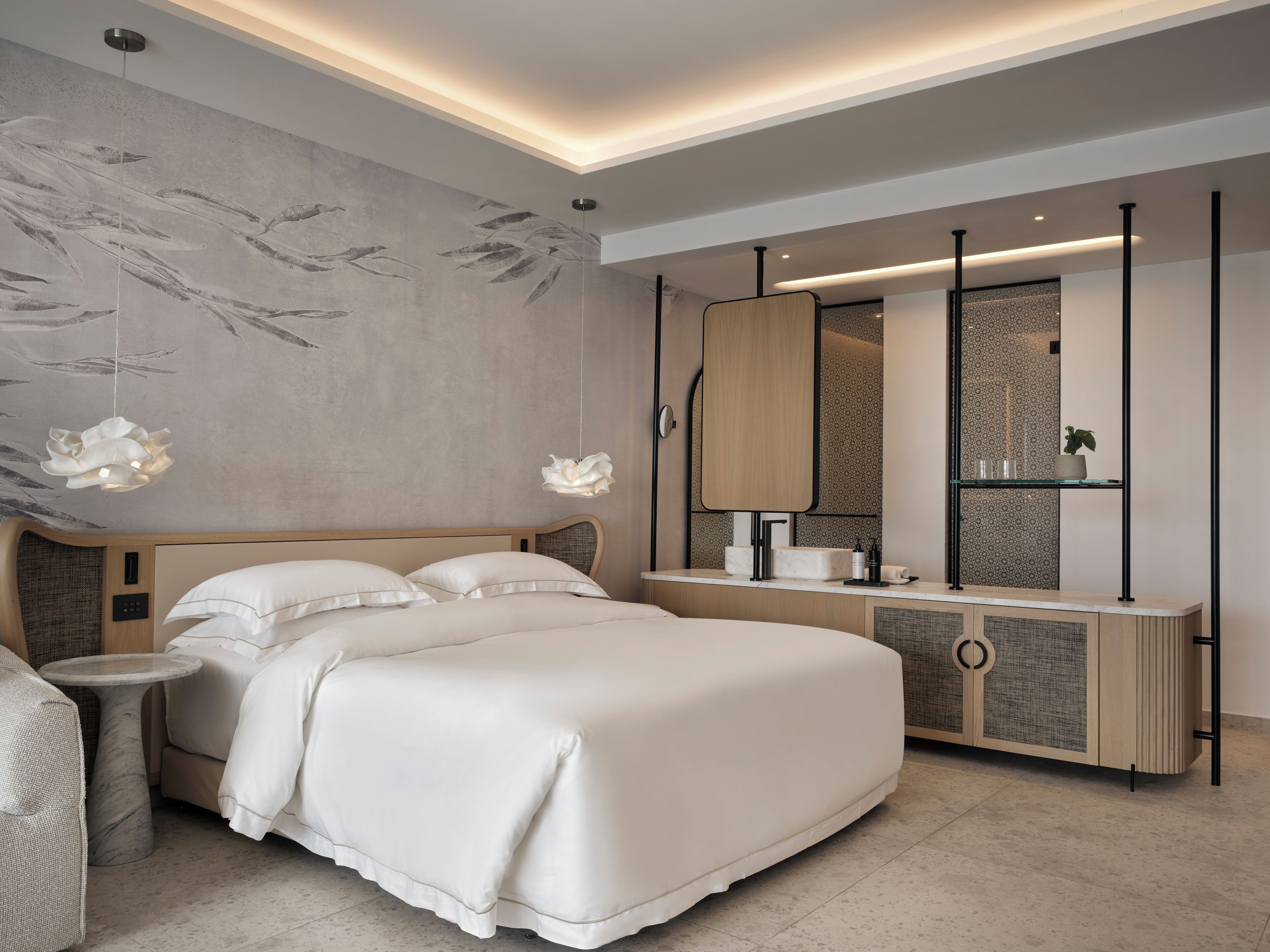 A modern bedroom with a large bed, bedside tables, a vanity with a mirror, and a wall with a leaf pattern.