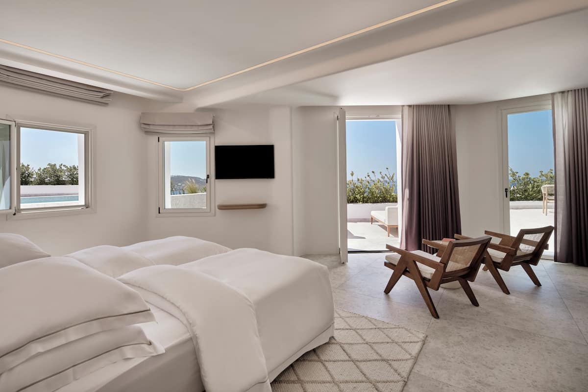 Une chambre d’hôtel moderne dotée d’un grand lit, d’un bureau avec des chaises, d’une télévision à écran plat et de grandes fenêtres offrant une vue sur l’extérieur.