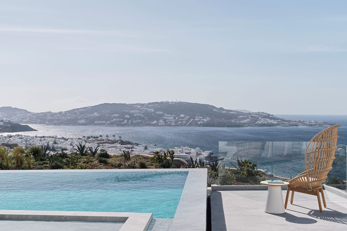 Un espace aménagé au bord de la piscine offrant une vue sur un paysage côtier, comprenant une colline et une étendue d’eau.