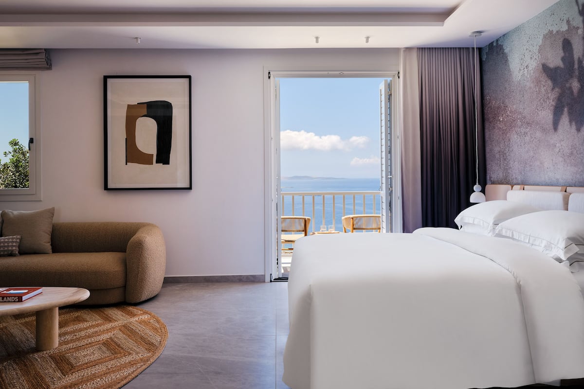 Une chambre d’hôtel moderne dotée d’un grand lit, d’un canapé, d’une petite table et d’un balcon offrant une vue sur la mer.