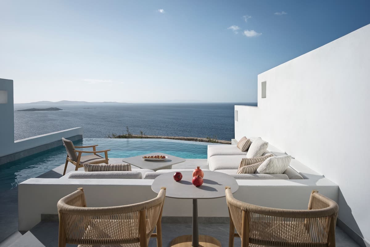 Un espace extérieur moderne, aménagé avec des sièges, une piscine, des murs blancs et une vue sur la mer.