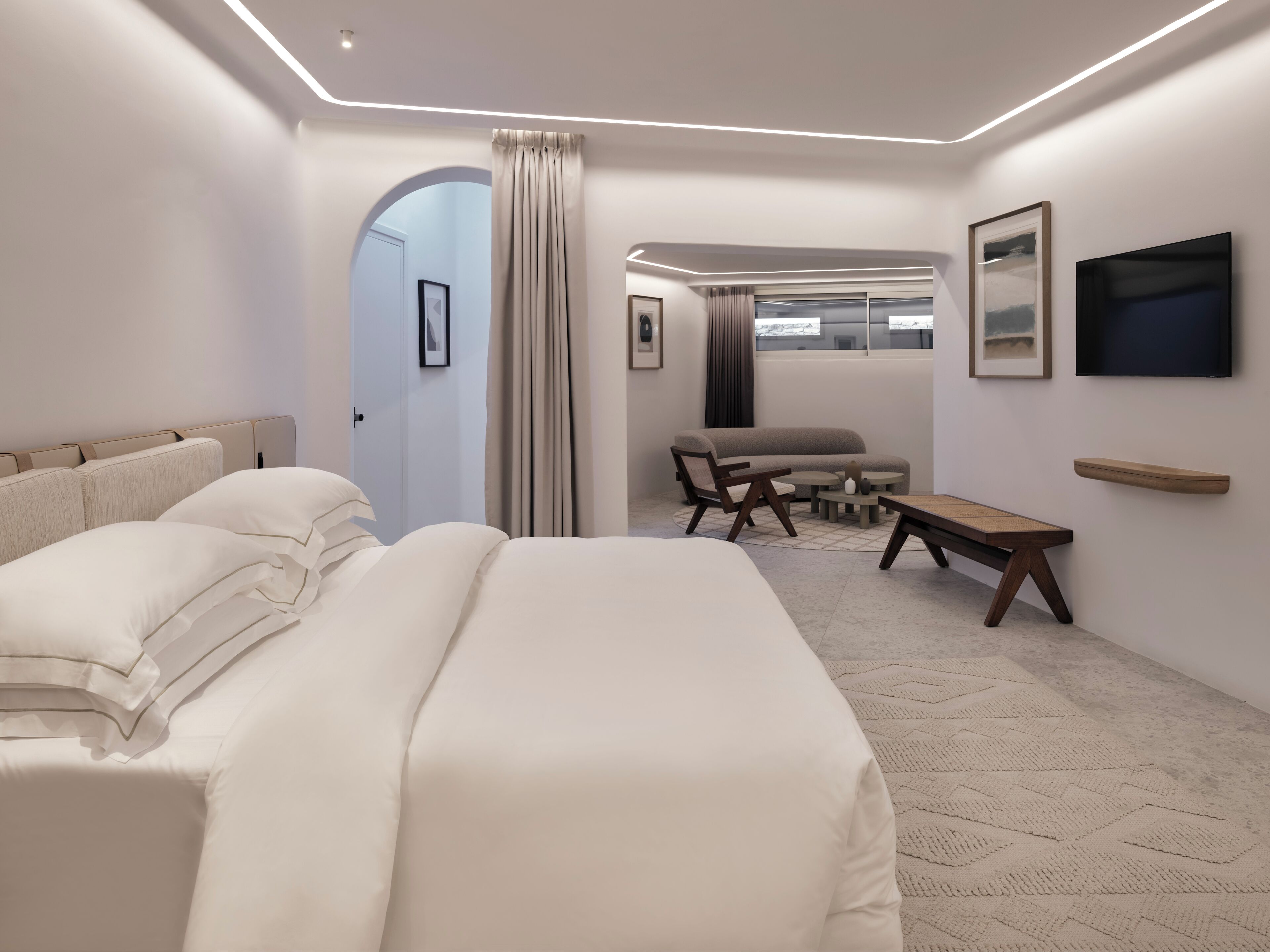 A modern hotel room with a large bed, a seating area with a table and chairs, and artwork on the walls.