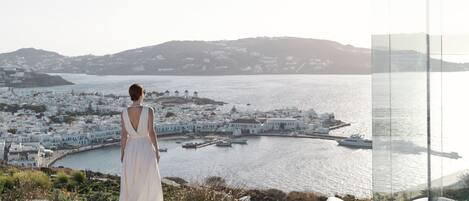 A woman in a white dress overlooking a coastal town with white buildings and boats in the harbor.