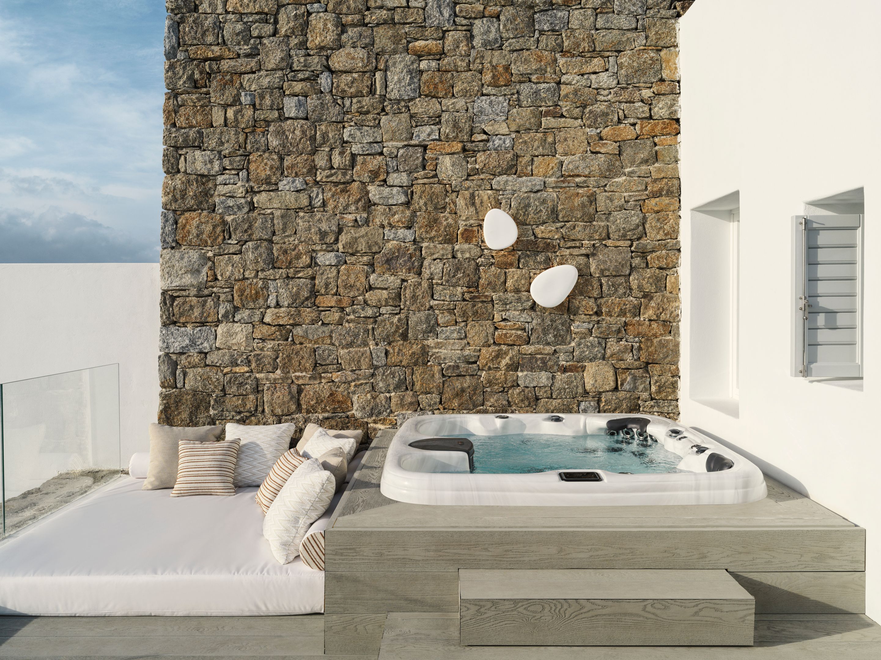 A modern outdoor seating area with a stone wall, a hot tub, and a sofa with cushions.