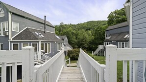 Een houten trap leidt naar een woongebied met huizen, een heldere lucht en een bebost heuvel op de achtergrond.